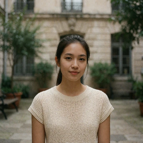 Malaysian woman in her mid twenties with hair tied back, standing in a quiet urban courtyard