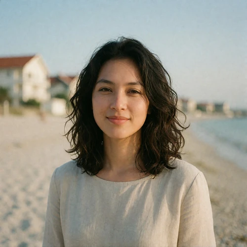 Malaysian woman in her late twenties with wavy dark hair, standing outdoors near seaside architecture, an example EasternSingles member profile photo